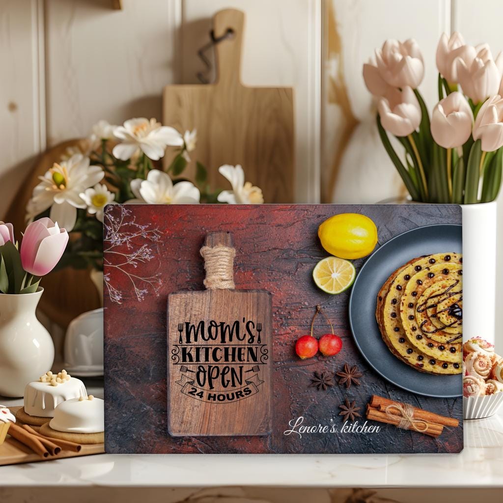 Rectangular glass chopping board with the phrase “Mom’s Kitchen Open 24 Hours” and personalized text at the bottom reading “Lenore’s kitchen.” Fun and custom kitchen gift.