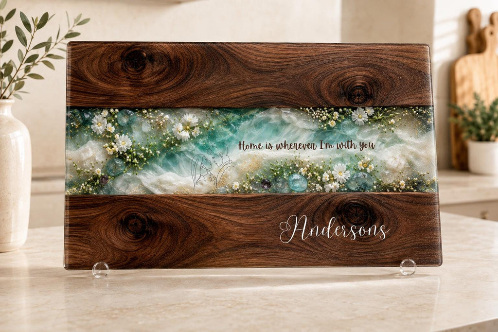 Personalised glass chopping board with dark wood and turquoise resin effect, white wildflowers and custom family name, decorative kitchen worktop saver and housewarming gift.