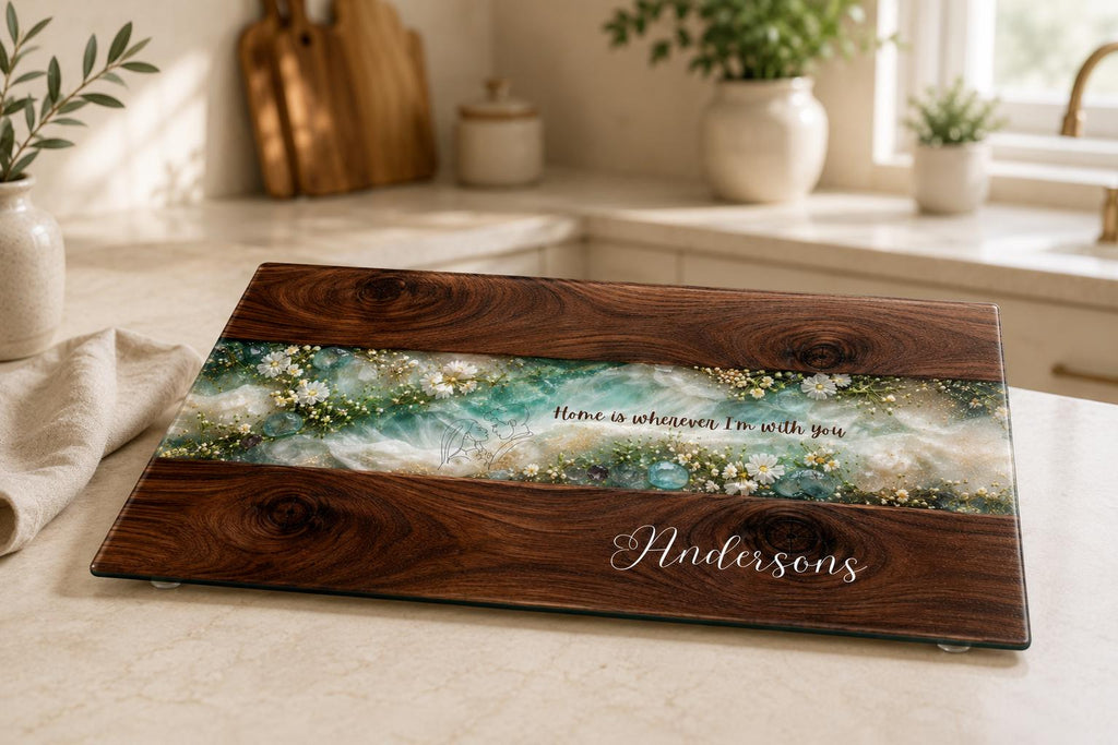 Personalised glass chopping board with dark wood effect, turquoise resin-style centre, white wildflowers and custom Andersons family name, displayed in a bright modern kitchen.
