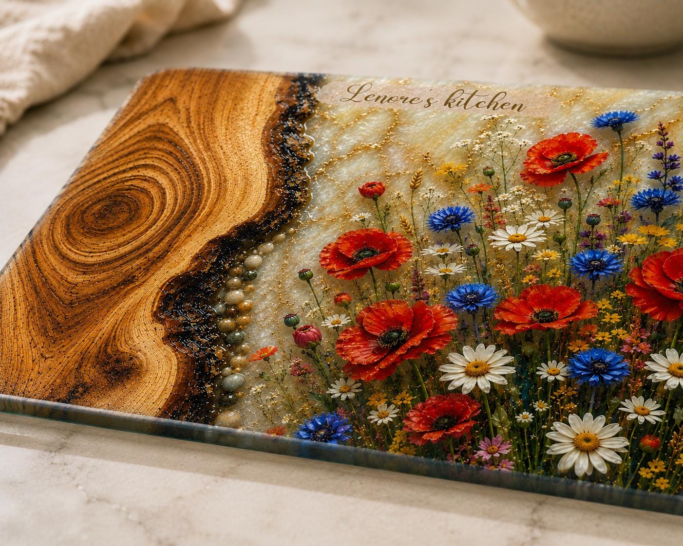 Personalised reinforced glass cutting board with epoxy resin style wood and wildflower design, 'Lenore's kitchen' text, and polished edges, displayed on a light kitchen countertop.